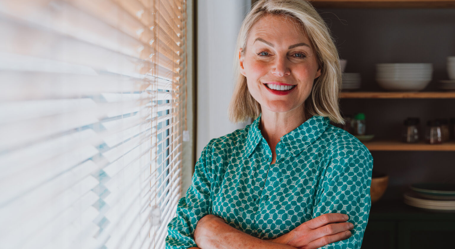Woman smiling by a window in her kitchen